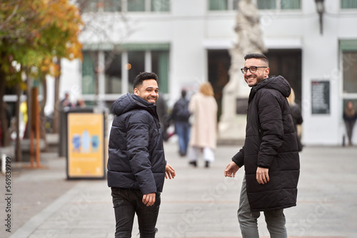 Two men looking at camera and smiling while walking outdoors on the street.