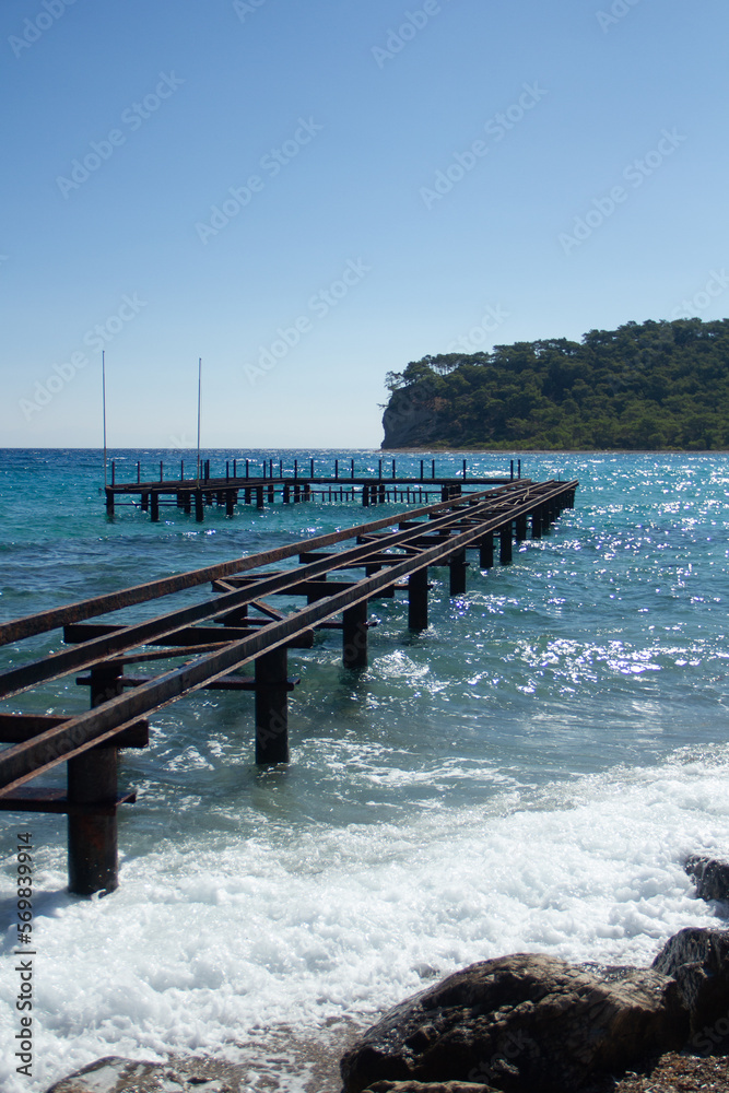 Iron pier for boats in the form of a breakwater on the coast of Turkey and the Mediterranean Sea against the backdrop of a coastal mountain