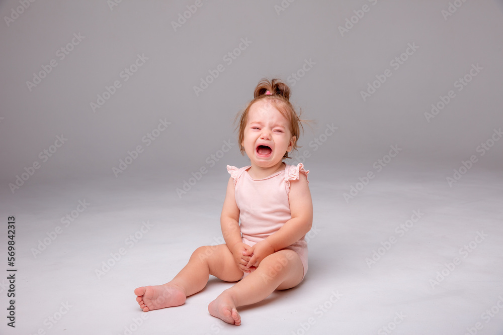 a baby girl in a pink bodysuit is sitting crying on a white background