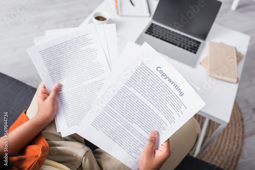 Top view of freelancer holding papers with copywriting lettering at home.