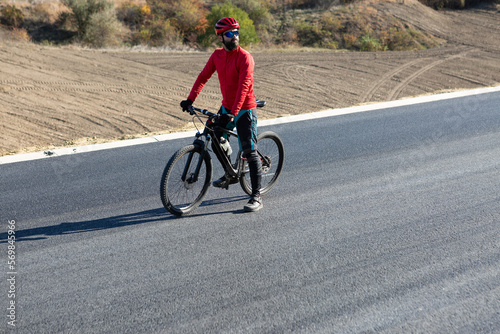 Cyclist riding bicycle on road against clear sky. A man in an outfit stands with a bicycle on an autumn sunny day.