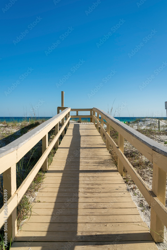 Boardwalk with shower station at the end against the beach and blue skyline background at Destin, FL. Pathway on a white sand with grasses.