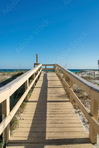 Boardwalk with shower station at the end against the beach and blue skyline background at Destin  FL. Pathway on a white sand with grasses.