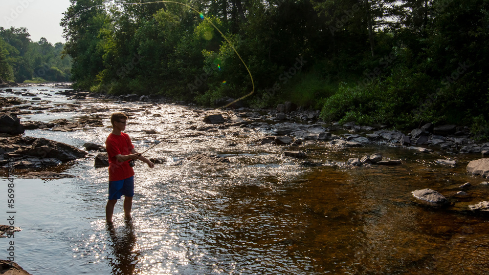 Teenage fly fisherman casting in peaceful stream on a summer day