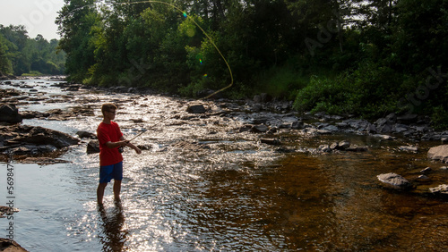 Teenage fly fisherman casting in peaceful stream on a summer day