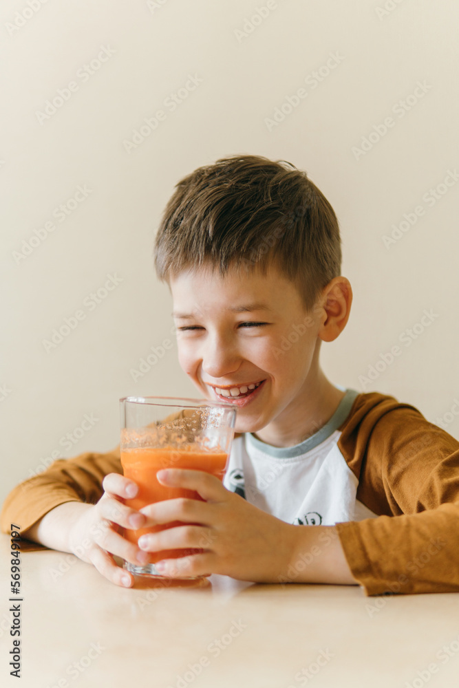 white boy drinks orange juice in the morning at the table and smiles white boy drinks orange juice in the morning at the table and smiles