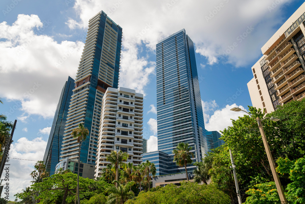 Large white puffy clouds above the condominium buildings with trees at Miami, Florida. Low angle view of trees and modern multi-storey residential buildings.