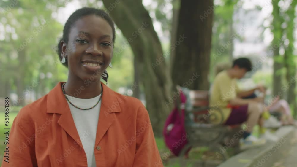 Portrait of African American gen Z girl smiling on camera while posing in park on summer day