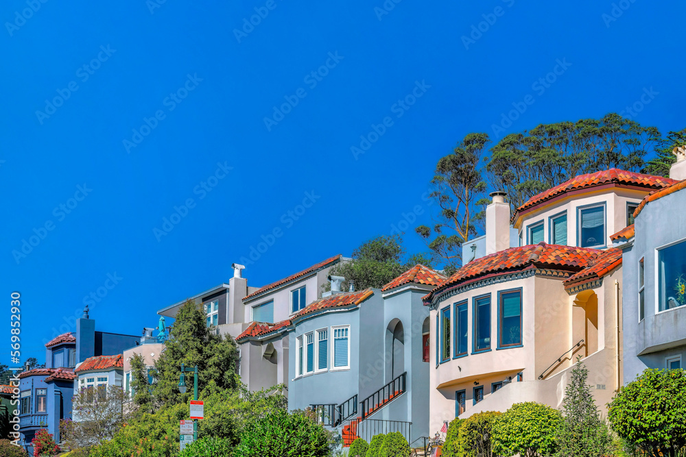 Houses in San Francisco neighborhood with blue sky on a sunny day. The homes have colorful exterior walls and ourdoor stairway leading to the intreior of the residence.