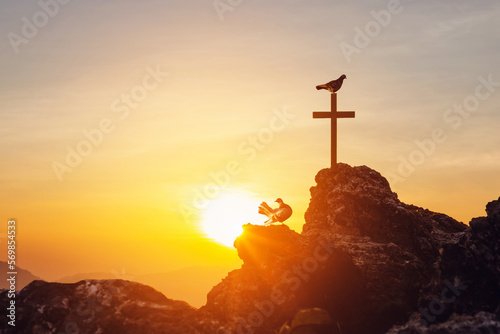 Silhouette Cross crucifix on top mountain hill and birds relaxing at sunset background. Christian praying in holy spirit religious.