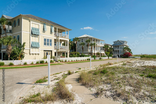 Sidewalk with white wood slats posts in a rich neighborhood at Destin, Florida. Concrete curved sidewalk near the white sand on the right and street on the left beside the fenced large houses. © Jason