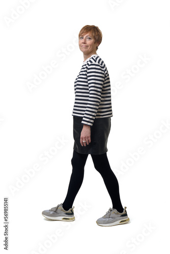 side view full length portrait of a woman in skirt, striped sweater and sneakers walking and looking at camera on white background