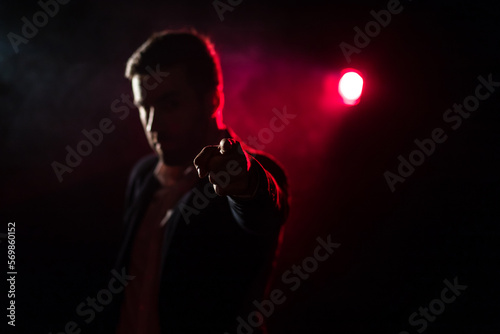 Photo of man showing thumb up on dark background with pink light. © Andrii