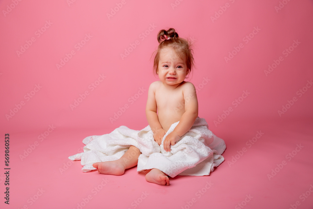 baby girl in a diaper wrapped in a towel sitting on a pink background, bathing concept