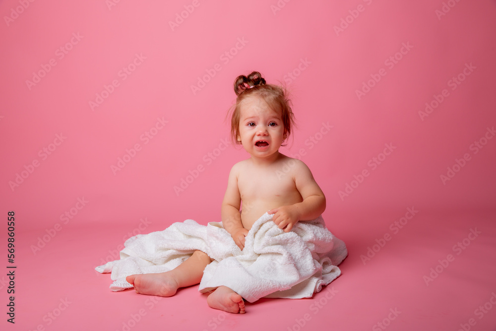 baby girl in a diaper wrapped in a towel sitting on a pink background, bathing concept