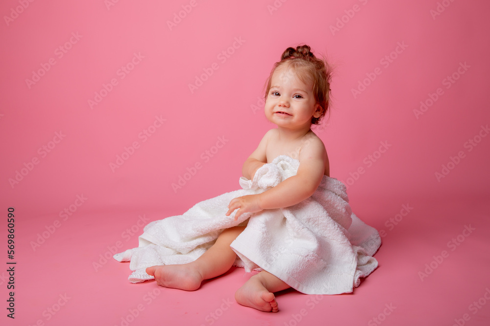 baby girl in a diaper wrapped in a towel sitting on a pink background, bathing concept