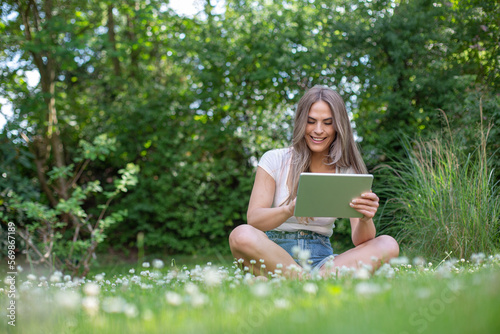 Young pretty blonde woman sitting in the garden with an tablet and reading, playing, online banking or using an app