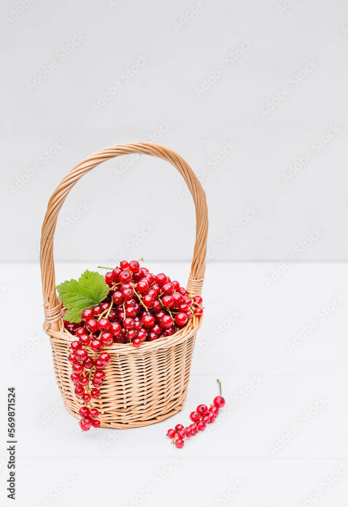A small wicker basket with fresh red currants on a white wooden isolated background. A beautiful, healthy ripe summer berry. A small wicker basket with fresh red currants on a white wooden isolated background. A beautiful, healthy ripe summer berry.
