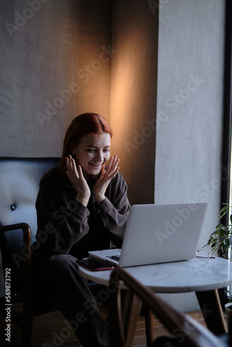 red-haired woman freelancer works remotely on laptop in cafe.