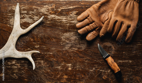 Reindeer antlers, leather gloves and a hunting knife on a rustic wooden table  - top view photo