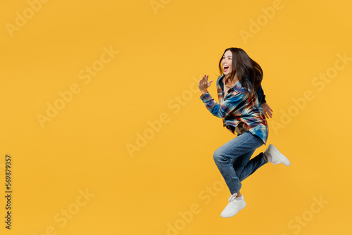 Full body side view young smiling excited caucasian fun woman wear blue shirt beige t-shirt jump high run fast hurry up isolated on plain yellow background studio portrait. People lifestyle concept.