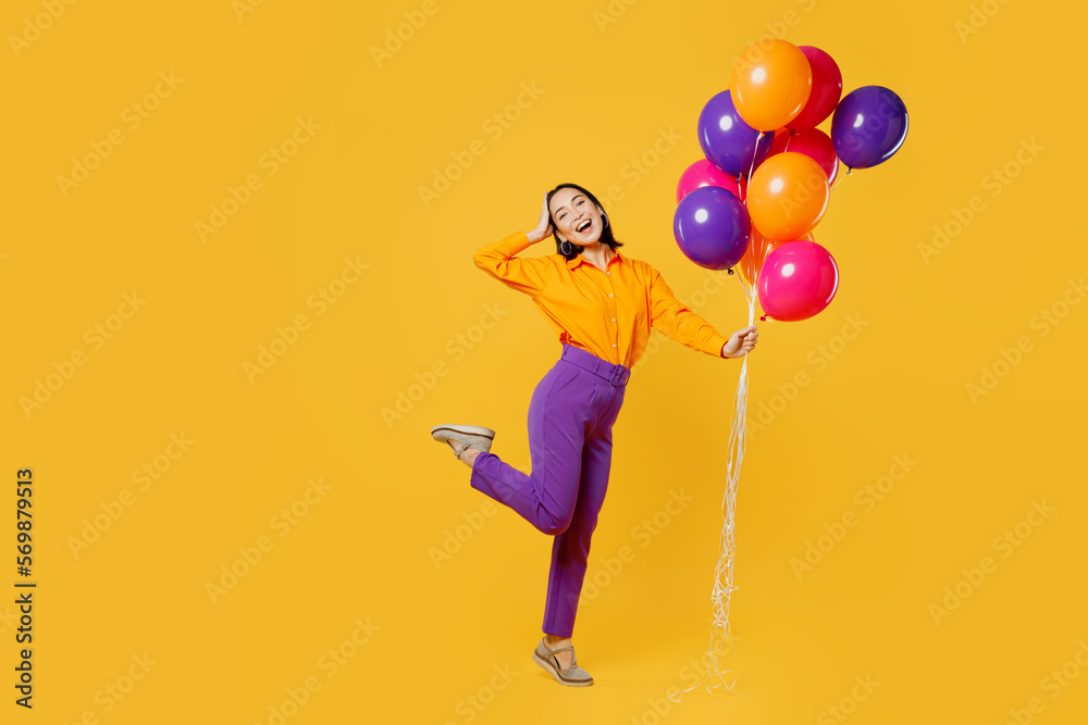 Full body cheerful side profile view happy fun young woman wear casual clothes celebrating hold head bunch of balloons posing isolated on plain yellow background. Birthday 8 14 holiday party concept.