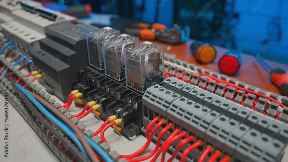 Electrical panel with many red and blue wires, electrical parts, automatic switches, breakers, residual current devices. Close up of a electrical switch and screwdriver on a table. Electrical panel with many red and blue wires, electrical parts, automatic switches, breakers, residual current devices. Close up of a electrical switch and screwdriver on a table.