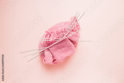 Pink yarn on a pink background. Knitting for a doll. Knitted sweater for a doll. Hobbies for girls.