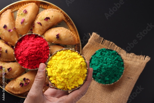 Holi Indian festival of colors celebrating with colorful Gulal Abeer mawa gujia mithai pirukiya sweets presented on a brass plate isolated on black background photo