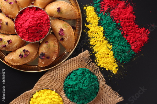Holi Indian festival of colors celebrating with colorful Gulal Abeer mawa gujia mithai pirukiya sweets presented on a brass plate and scattered isolated on black background photo