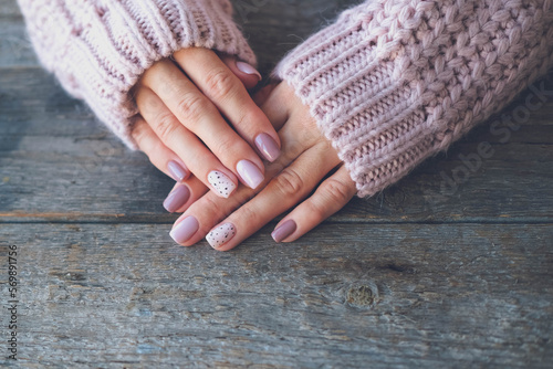 Women is hands with a beautiful manicure  on a wooden background. Autumn trend, polish the beige and quail egg pattern on the nails with gel polish, shellac. Copy space.