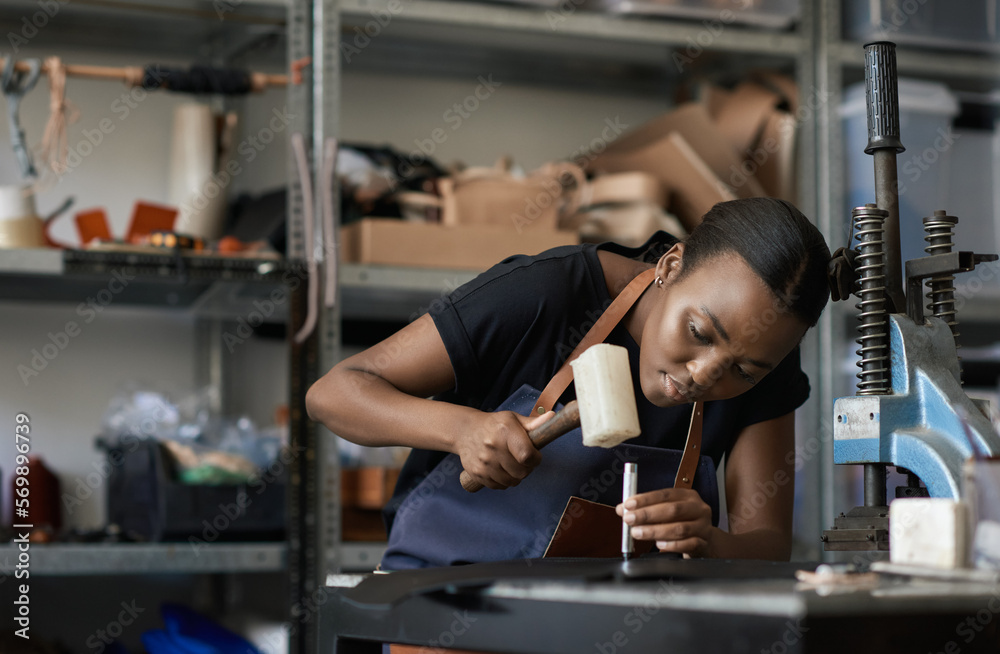 Young African female leather worker using a mallet and punch Young African female leather worker using a mallet and punch