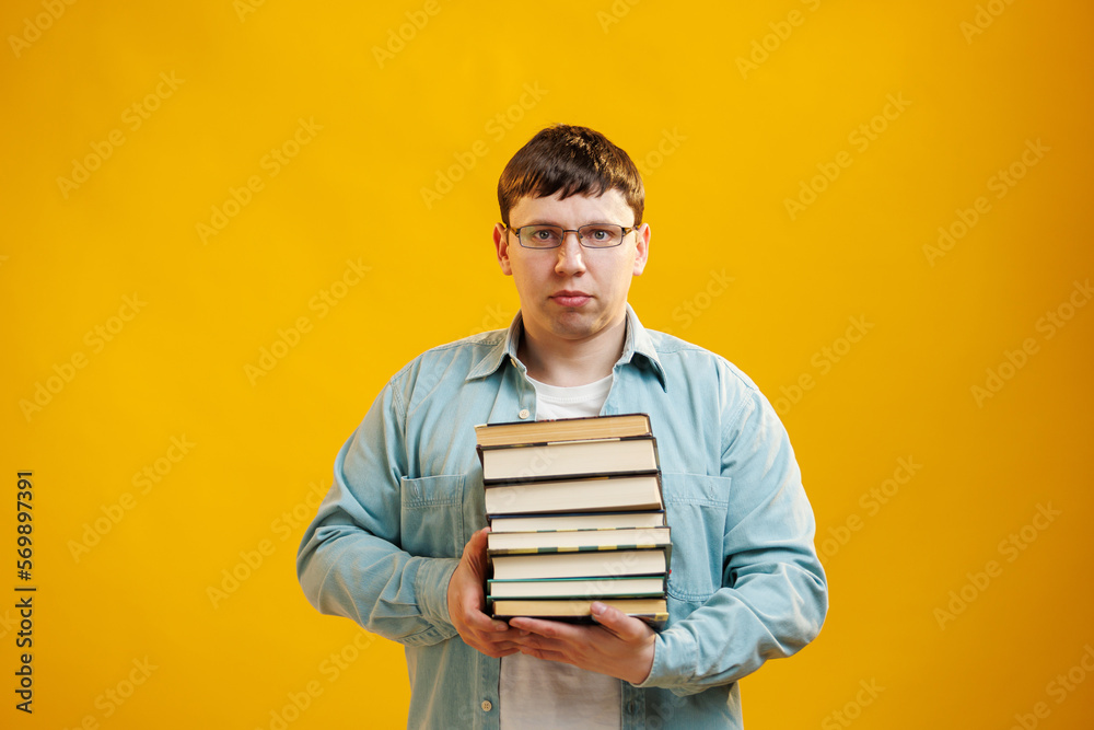 Young man student in glasses holds stack of university books from college library on yellow background. Happy guy smiles, he is happy to graduate, education abroad concept. Copy space Young man student in glasses holds stack of university books from college library on yellow background. Happy guy smiles, he is happy to graduate, education abroad concept. Copy space