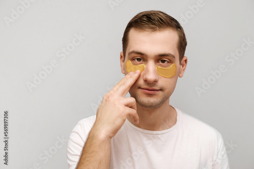 Close up photo of serious man in white t-shirt with patches under eyes looking at camera. Beauty routine, cosmetic concept