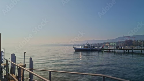 Panning of beautiful landscape with Lake Zürich, pier, ships, quay bridge and skyline at City of Zürich on a sunny winter day. Movie shot February 9th, 2023, Zurich, Switzerland.