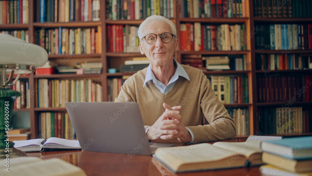 Portrait of friendly senior man working on laptop in library, doing research Portrait of friendly senior man working on laptop in library, doing research