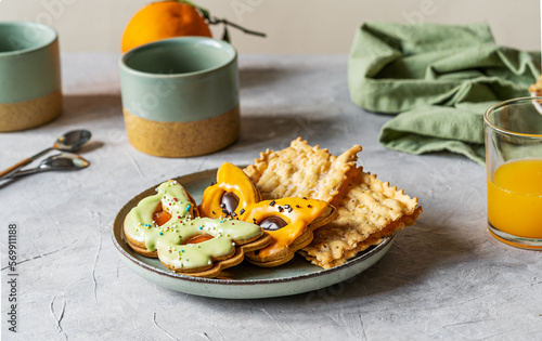 Carnival sweets in shape of carnival mask green and orange colour, mugs, orange fruit and juice, carnival fritters or bugie on light grey background photo