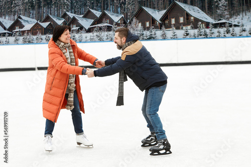 Vacation. Middle-aged couple, man and woman having fun outdoors, skating on open air ice rink in winter day. Concept of leisure activity, winter hobby and sport, vacation, fun, relationship, emotions.