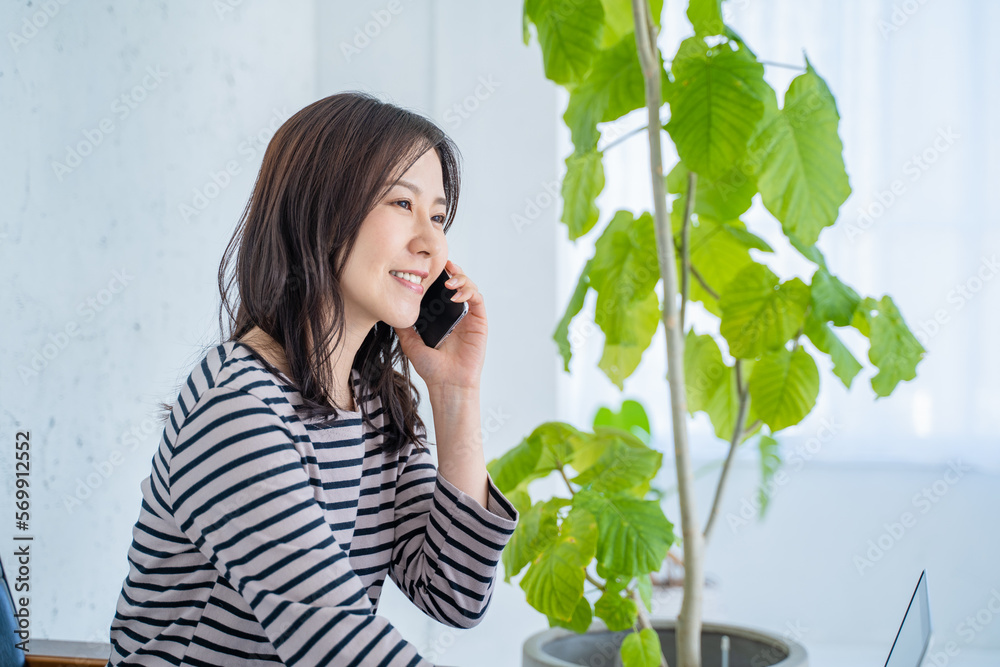 明るいリビングでソファに座りスマホで通話をする女性 明るいリビングでソファに座りスマホで通話をする女性