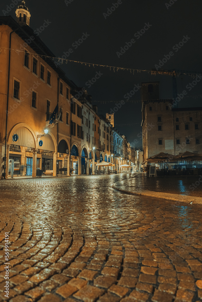 Mantua city center during an autumn night with the wet street between shops and Piazza delle Erbe - Mantova