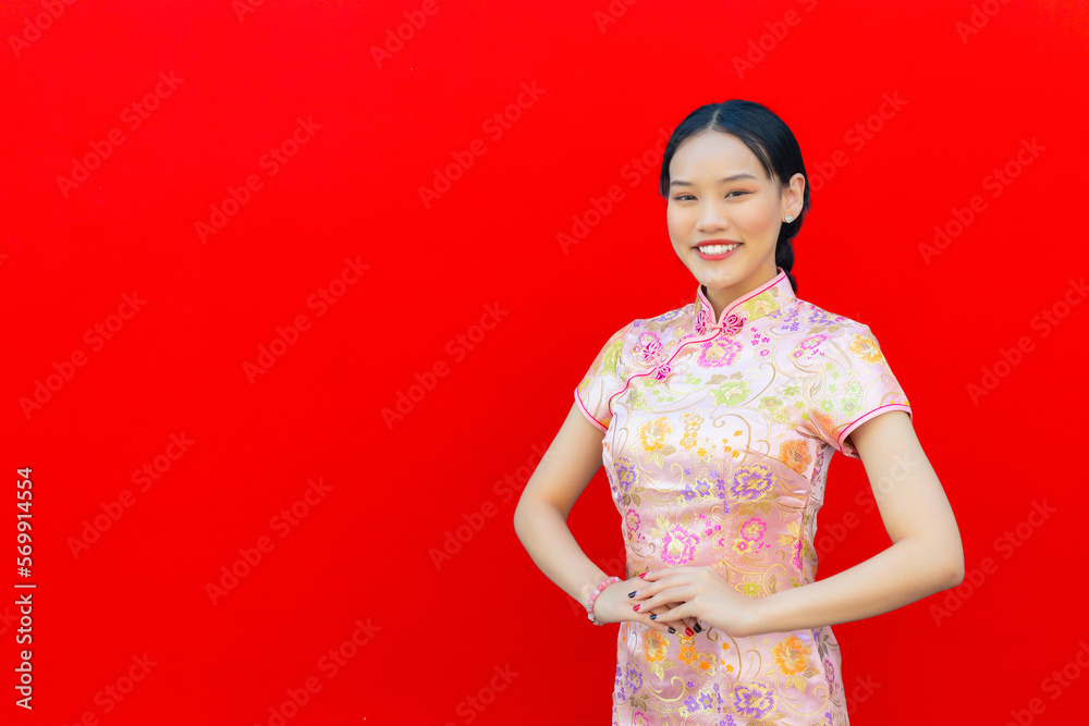 Beautiful Asian woman with long hair who wears pink Cheongsam dress in Chinese new year theme while she shows her hand as Chinese greeting with on red background. Beautiful Asian woman with long hair who wears pink Cheongsam dress in Chinese new year theme while she shows her hand as Chinese greeting with on red background.