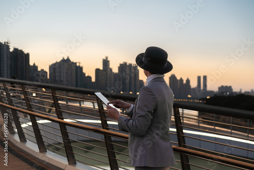 Asian businessman is using tablet outdoors in front of the city buildings at blue time.