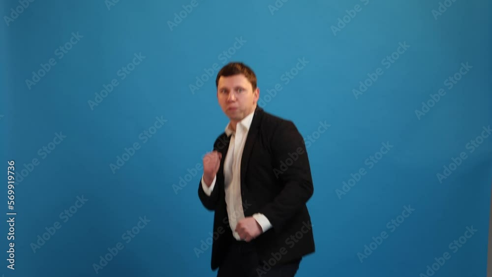Businessman standing with boxing gesture, punching to camera, provoking fight or ready to self-defense, wearing suit on blue studio background Businessman standing with boxing gesture, punching to camera, provoking fight or ready to self-defense, wearing suit on blue studio background