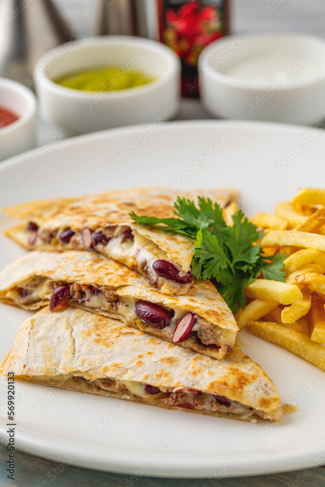 Mexican quesadilla with sauce and french fries on a white porcelain plate