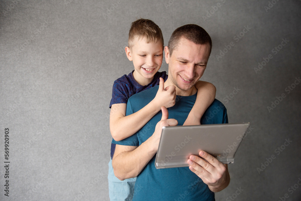 Cute boy hugs dad from behind, talking on a video link in a tablet