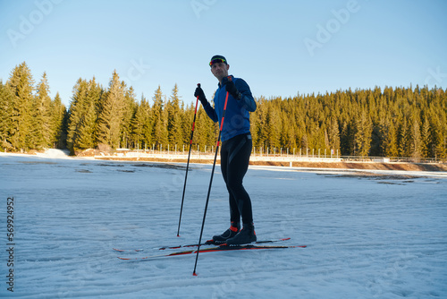 Handsome male athlete with cross country skis preparing equipment for training in a snowy forest. Checking smartwatch. Healthy winter lifestyle.