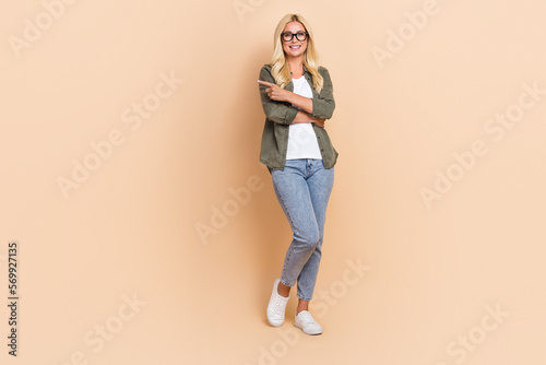 Full length photo of stunning positive lady wear trendy clothes arm direct empty space special offer isolated on beige color background