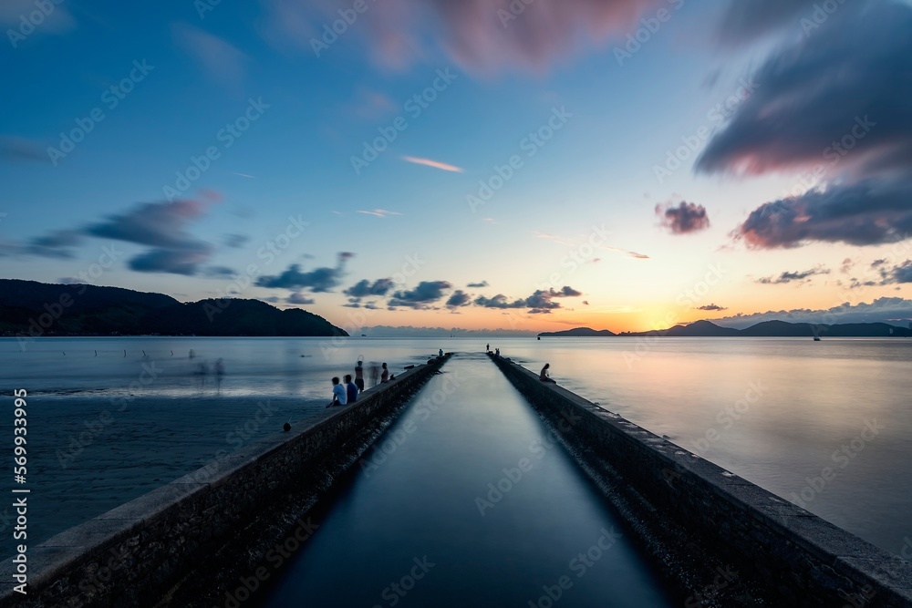 Santos city, Brazil. Sunset at the end of the beach. Water Channel nº6. People enjoying the beach on the short wall. Long exposure photography.