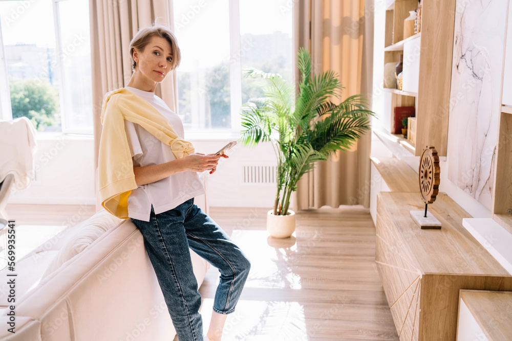 Middle age female using smartphone while leaning on sofa at home