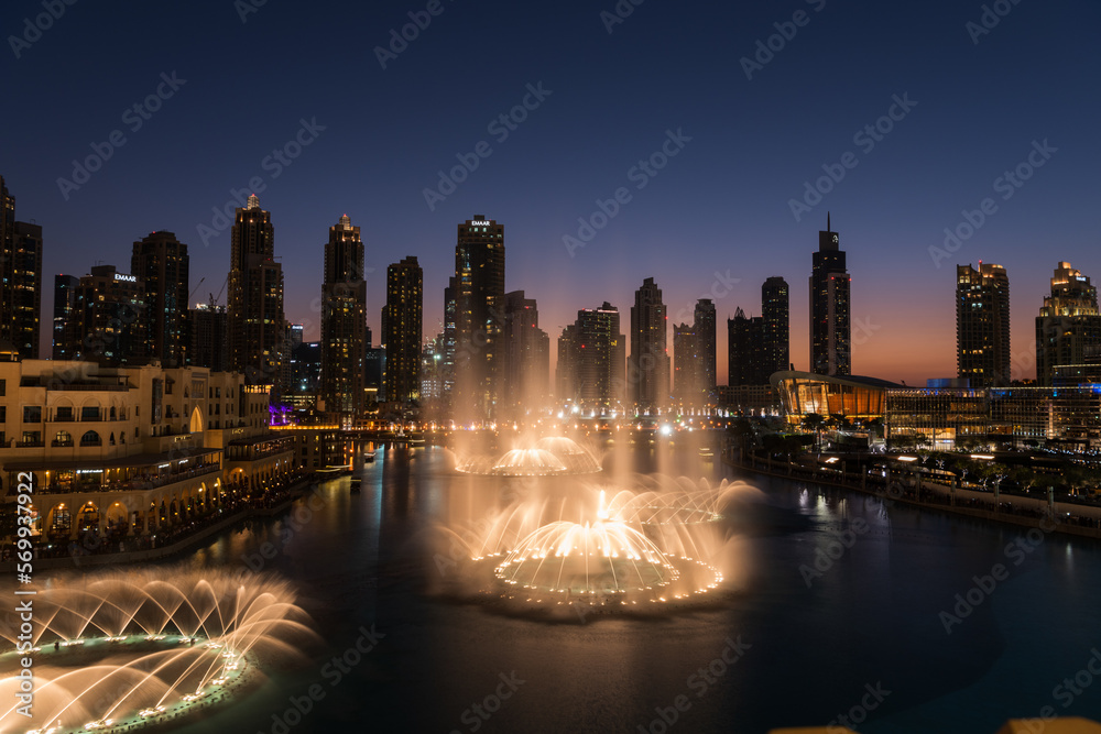 Obraz premium Dubai singing fountains at night lake view between skyscrapers. City skyline in dusk modern architecture in UAE capital downtown.